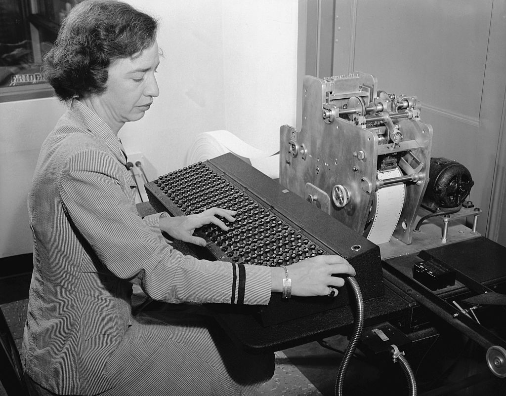 Lieutenant Grace Hopper codes problems onto punch tape for feeding into a new calculating machine invented by Commander Howard H. Aiken, USNR. The calculator will be presented to Harvard University by IBM Corporation, for use by the US Navy for the duration of the war. The machine is a revolutionary new electrical device of major importance to the war effort. It will explore vast fields in pure mathematics and in all sciences, previously barred by excessively intricate and time-consuming calculations. Two years of research were required to develop the basic theory behind the giant calculator. Six years of design and construction and testing were necessary to transform Commander Aiken's original conception into the completed machine at the engineering laboratory of IBM in Endicott, N.Y.
