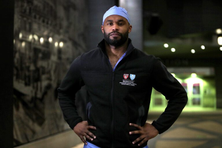 Myron Rolle stands outside at night wearing his scrubs with his hands on his hips