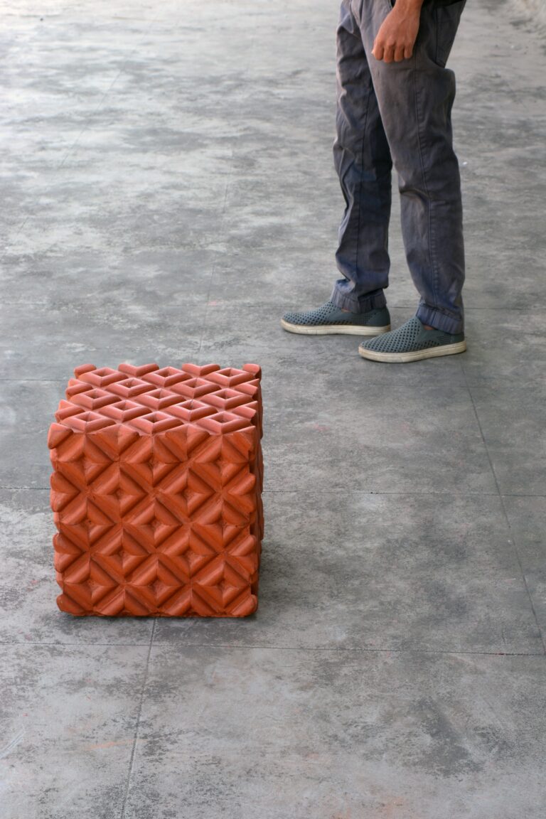 a person's legs are shown standing to the side of a cube-shaped chair made from recycled clay roofing