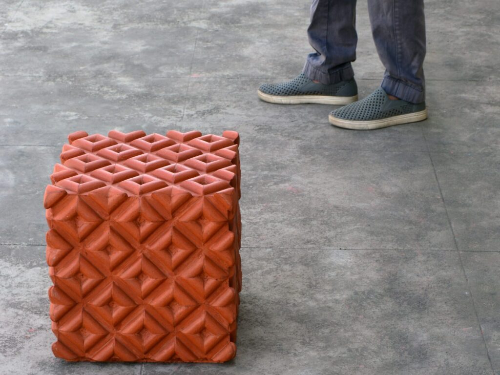 a person's legs are shown standing to the side of a cube-shaped chair made from recycled clay roofing