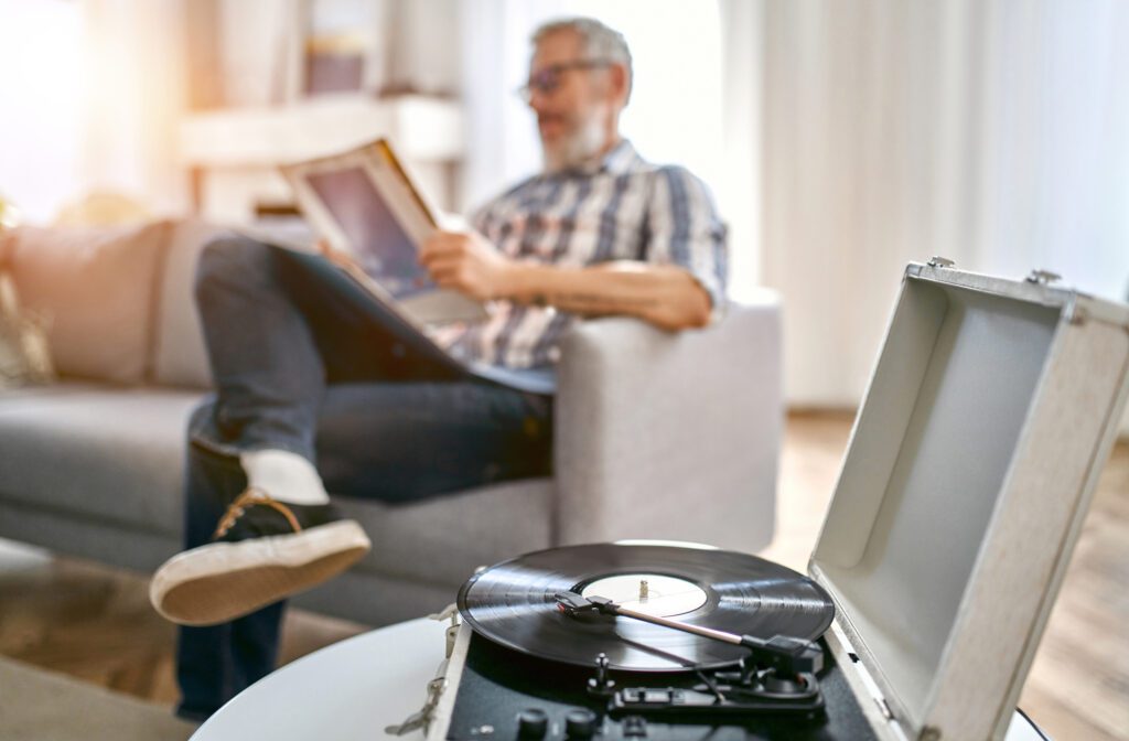 a record spins on a turntable in the foreground as an older man relaxes in an armchair in the background