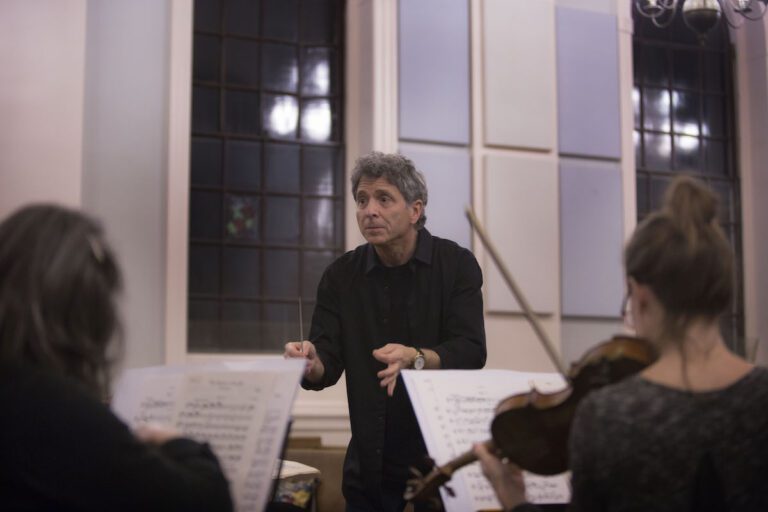 Ronald Braunstein intently conducts an orchestra in front of an open window