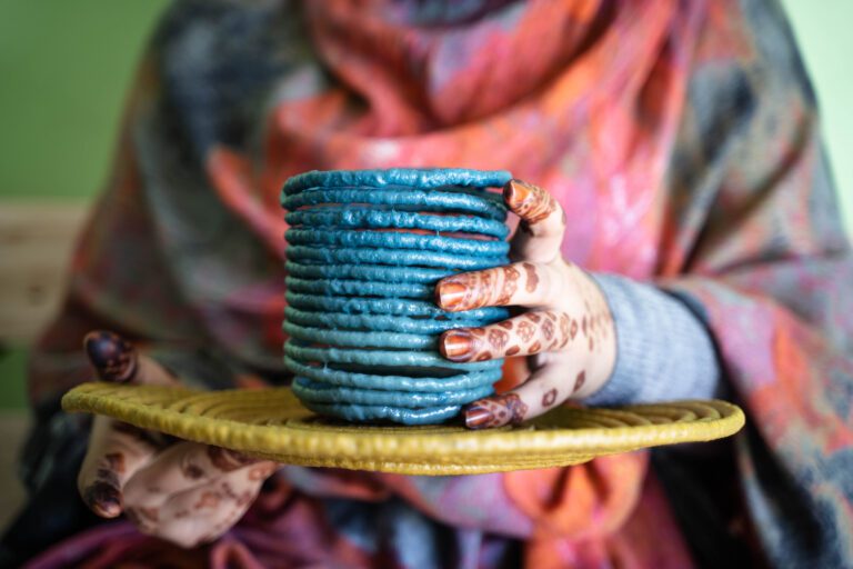 A woman in a refugee camp holds a bright colored pot made from recycled plastics