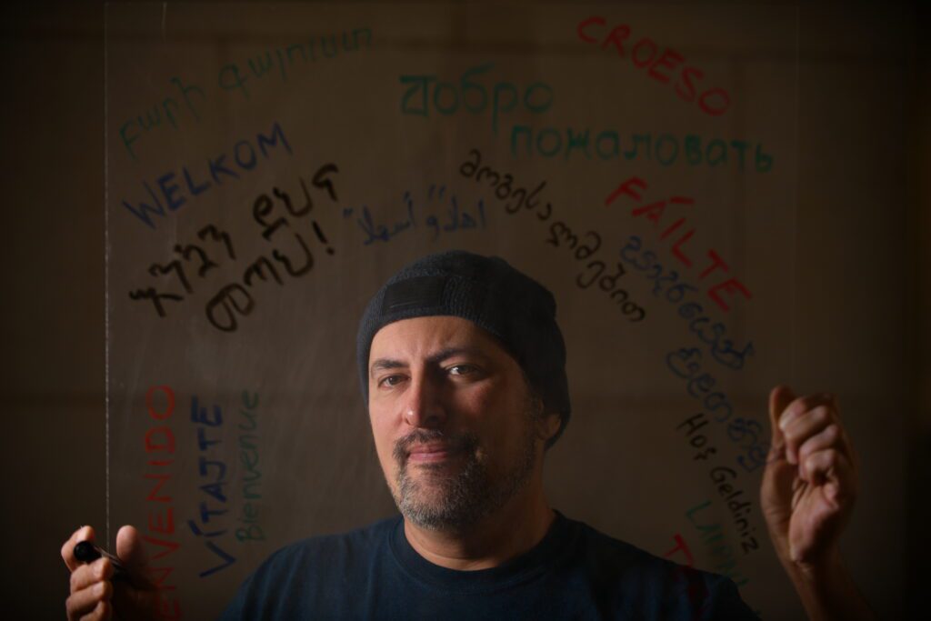 Carpet cleaner Vaughn Smith wears a beanie and looks at camera with a small smile in front of a wall featuring different written languages
