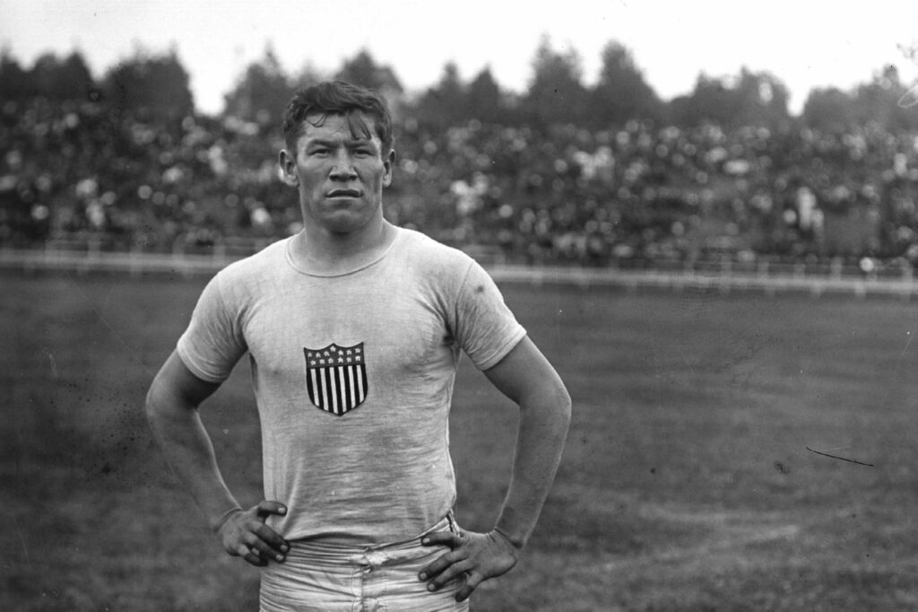 Jim Thorpe stand on field looking at camera with arms on hips at an athletics meeting at the Parc Pommery in Reims, France, 23rd July 1912.