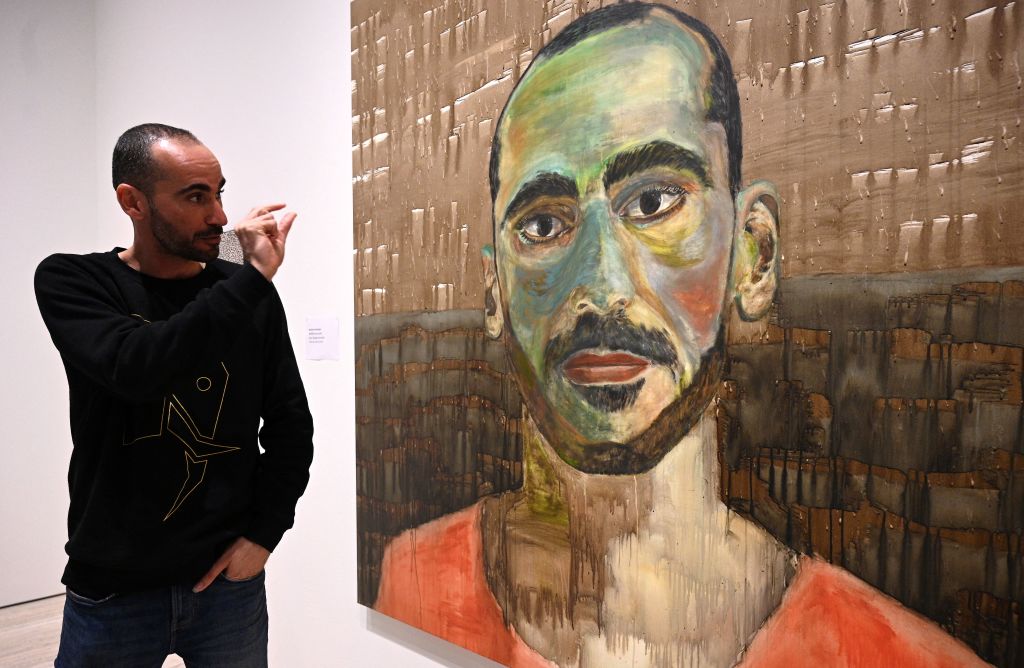 Mostafa Azimitabar stands next to the art he created with a toothbrush and coffee