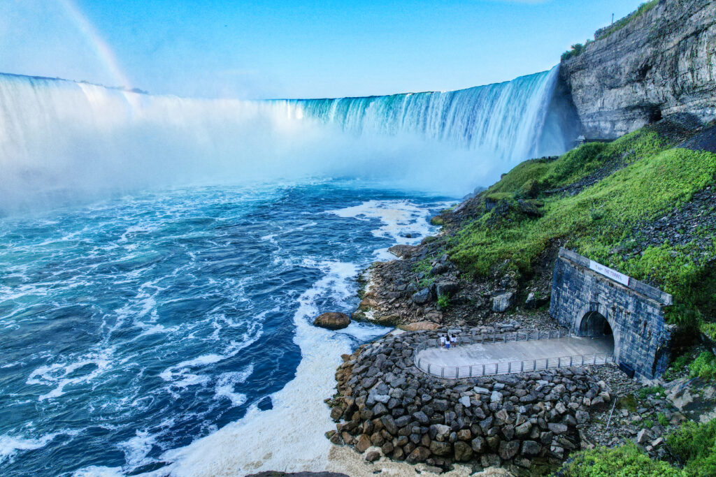 a drone shot of the niagara falls with one entrance to the tunnel carved into the landscape in the foreground