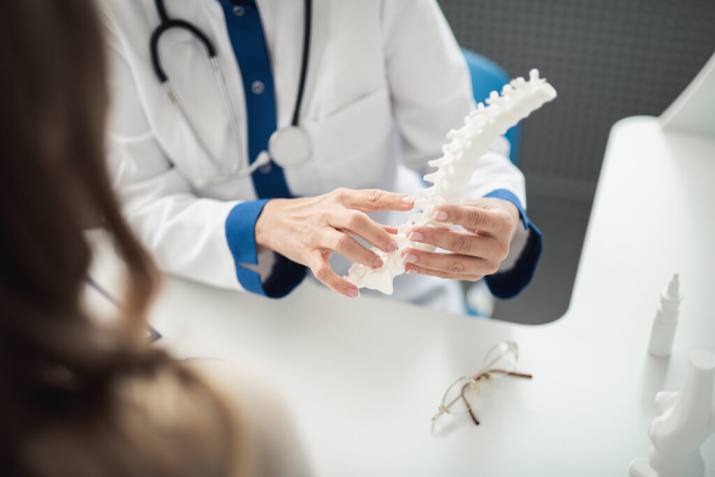 Close up portrait of female doctor showing medical spine model to young lady in clinic