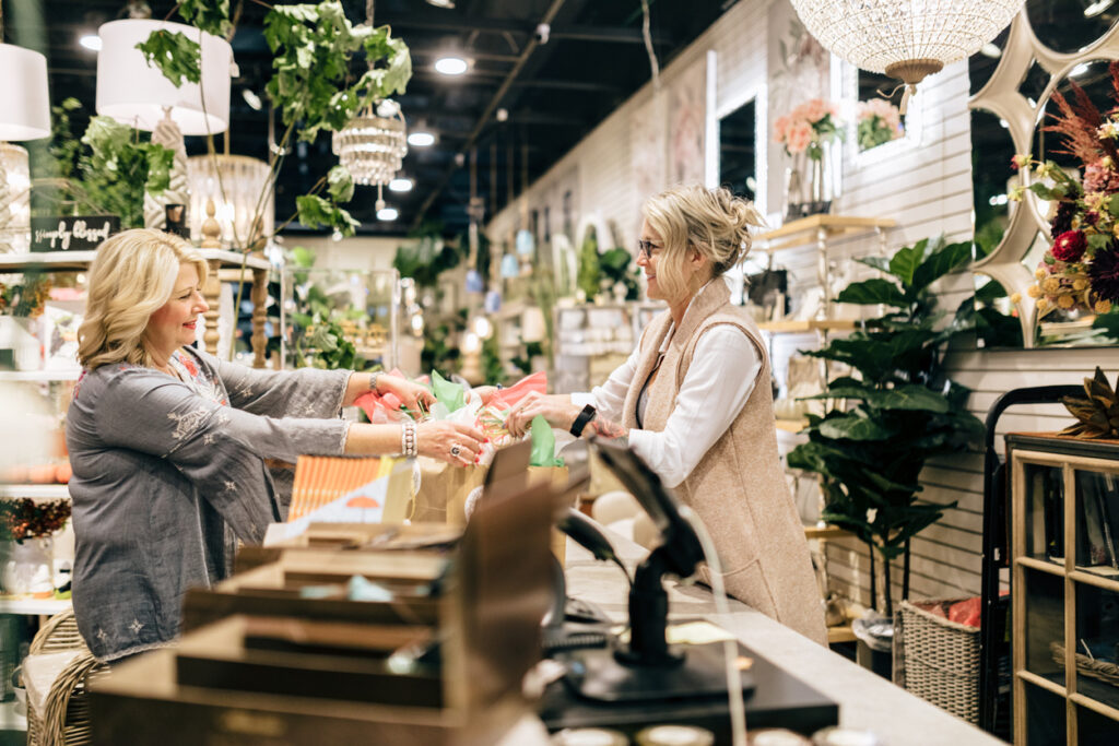 A mature adult caucasian woman hands a customer her shopping purchase at a home retail store.