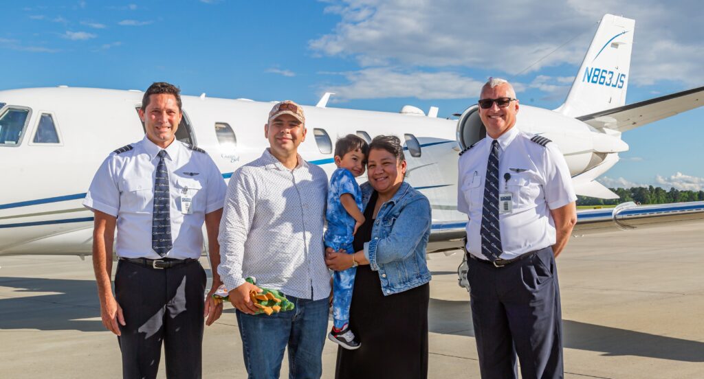 two pilots and a family with a small child stand happily outside a private AeroAngel jet