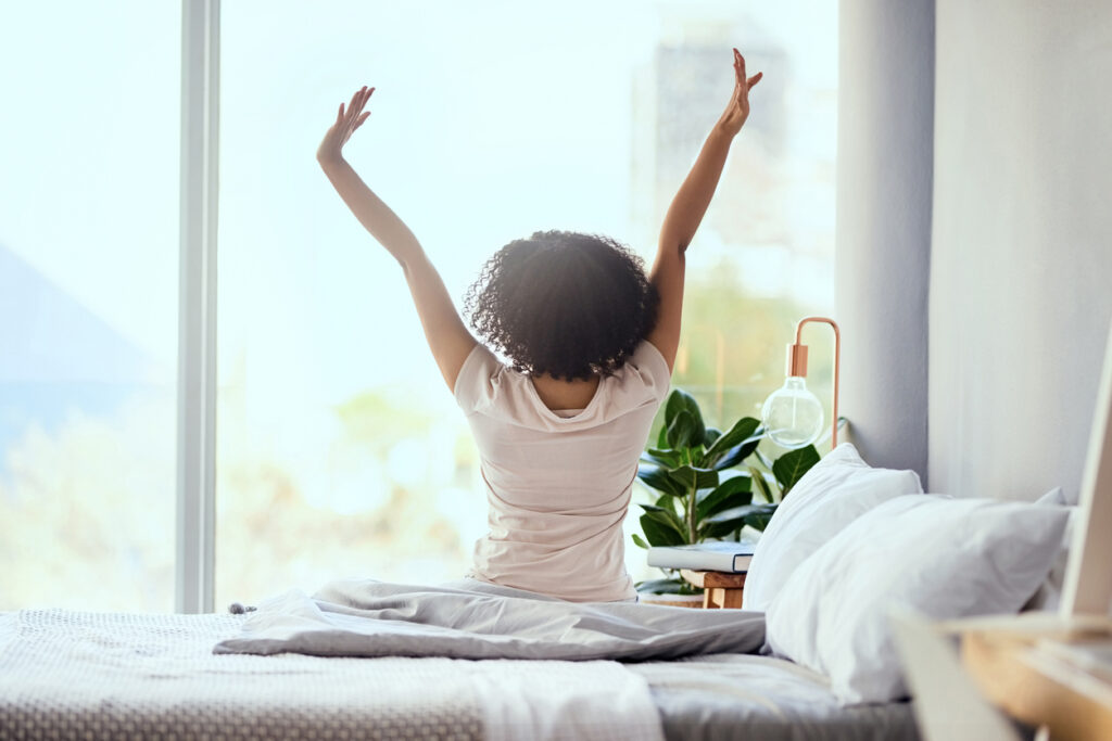 Shot of a young woman sitting on the bed in the morning and stretching