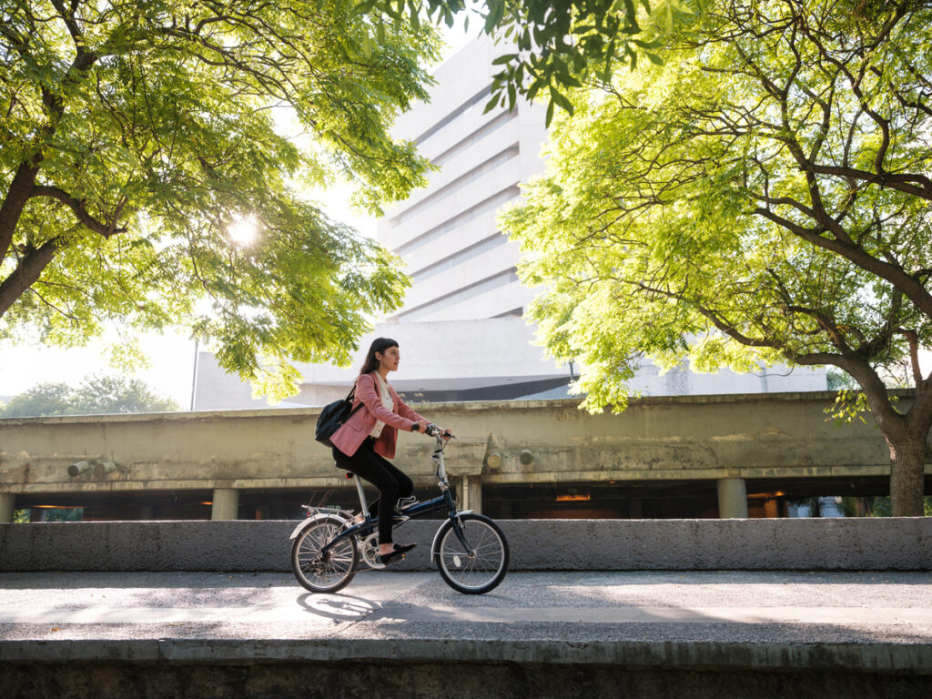 A young woman riding her bike in the city with trees behind her.