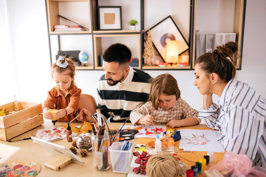 Young beautiful family with two children drawing at home, an examples of one of the indoor activities on the list.