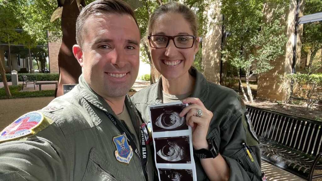 U.S. Air Force Maj. Lauren Olme stands with her husband and holds up an ultrasound. They are both smiling and dressed in uniform.