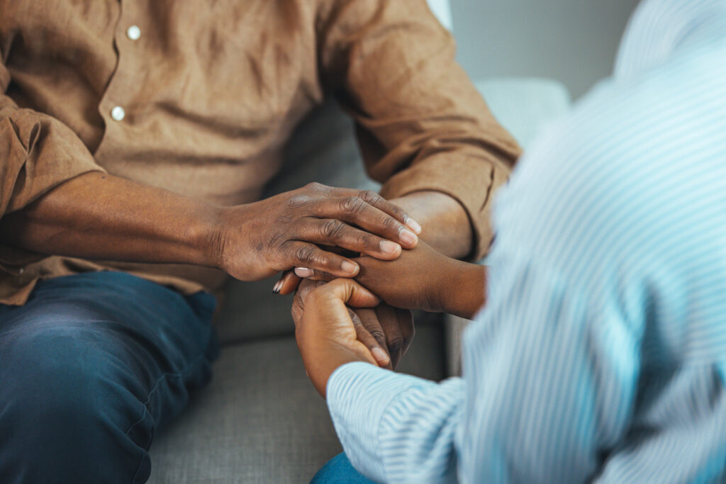 Close up of a black woman and man sitting on couch holding hands in forgiveness.