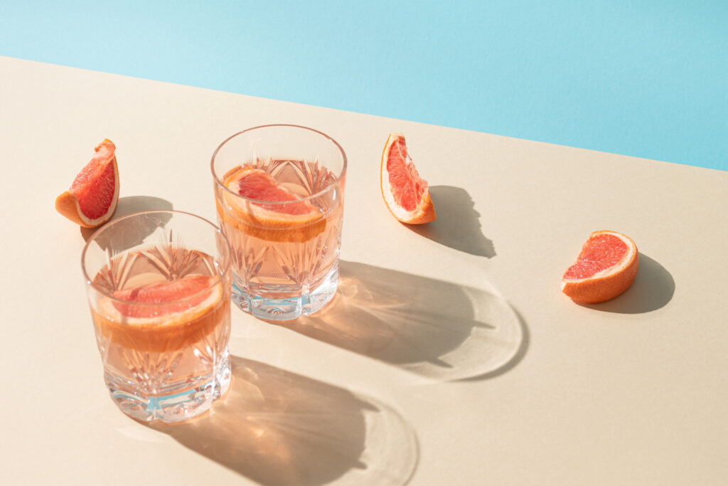 Two glasses of drink with slices of fresh grapefruit against bright beige and blue background.