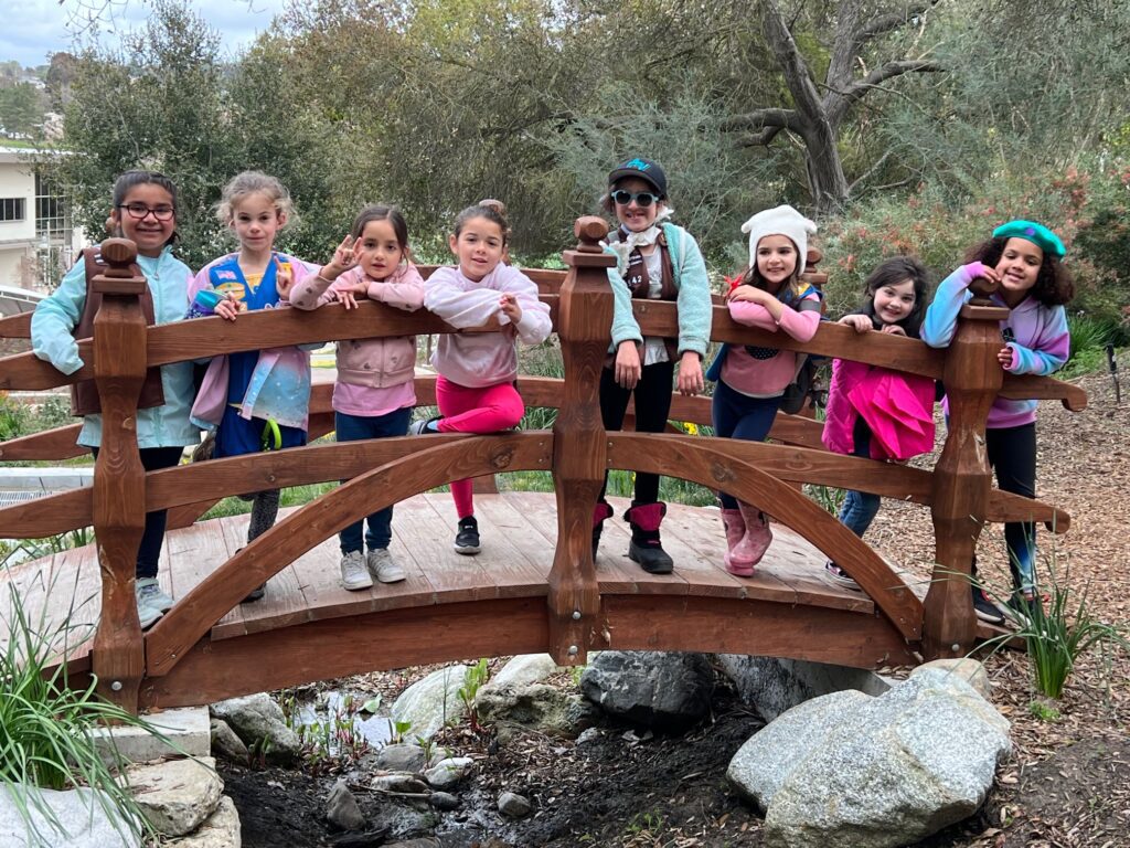 members of Girl Scout Troop 8542, which brings together kids and their families who are part of the deaf community, stand on a bridge with big smiles
