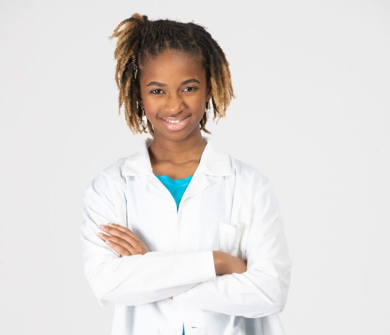 Alena Aleigh smiles and looks at the camera with arms crossed in a white lab coat