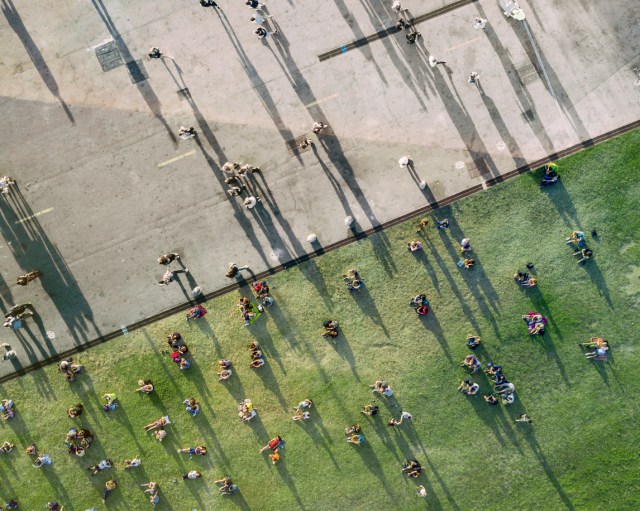 An aerial view of people sunbathing in the park, some on the cement and the others on the grass