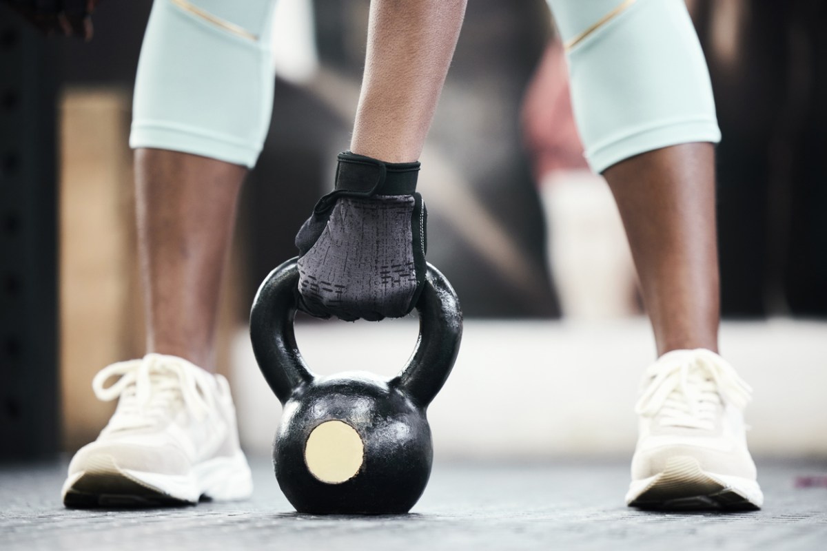 photo of an unidentified woman bending down with one hand about to lift a kettlebell weight