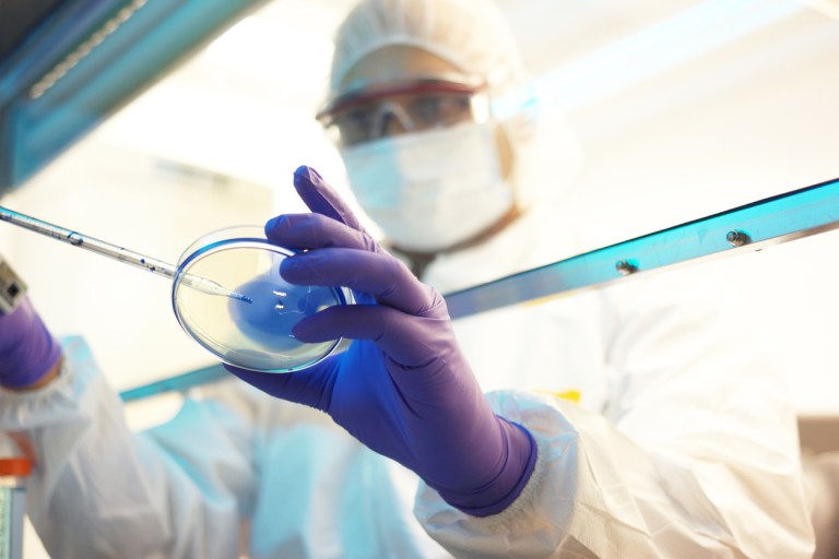 view from underneath: a scientist in protective gear examines a petri dish