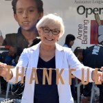 actress Ann Benson stands in front of an Operation School Bell sign and holds up a string of letters that say "Thankful" during filming of the Assistance League documentary A Pebble in the Pond