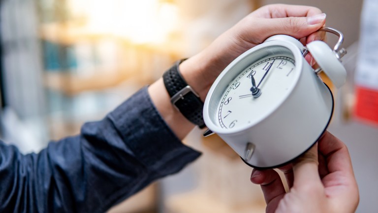 Male hand adjusting or changing the time on white clock.