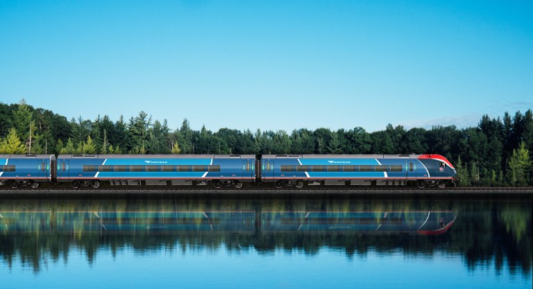 an image of a new, sleek, amtrak train moving across an area with blue water and trees