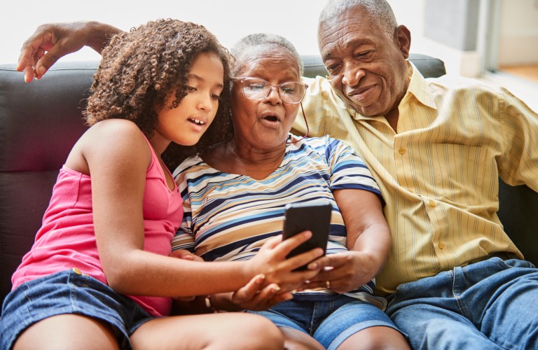 Shot of an adorable little girl showing viral videos on mobile phone to her grandparents at home