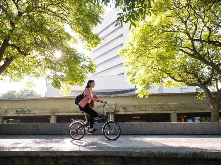 A young woman riding her bike in the city with trees behind her.