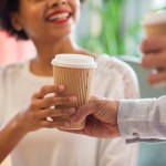 close up of happy african american woman hand taking coffee cup from man on random acts of kindness day