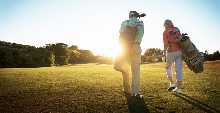 Shot of a retired couple walking across a golf green