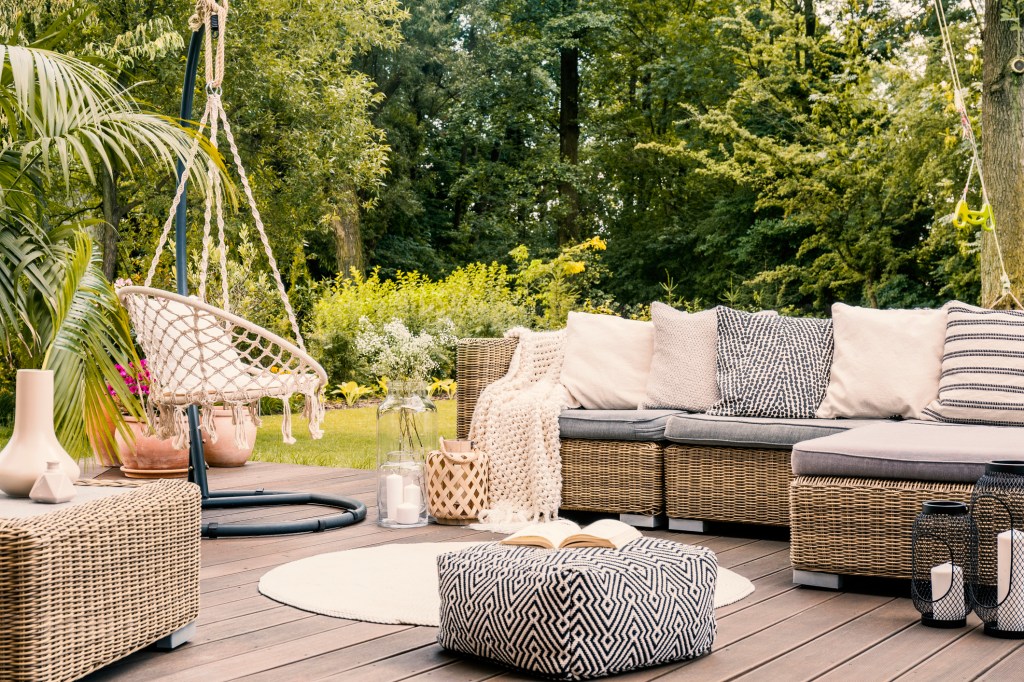 Book on a black and white pouf in the middle of a bright terrace with a rattan corner sofa, hanging chair and round rug. Real photo KatarzynaBialasiewicz/ iStock